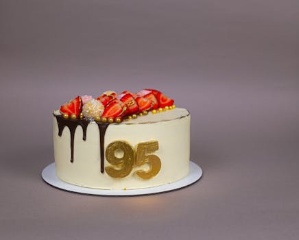 Gâteau d'anniversaire praliné-chocolat décoré de fraises et de chiffres dorés 95 sur un fond neutre.