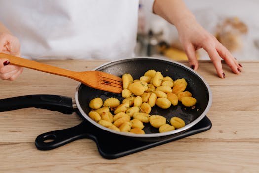 Gnocchis dorés dans une poêle en train d'être mélangés avec une spatule en bois sur un plan de travail en bois.