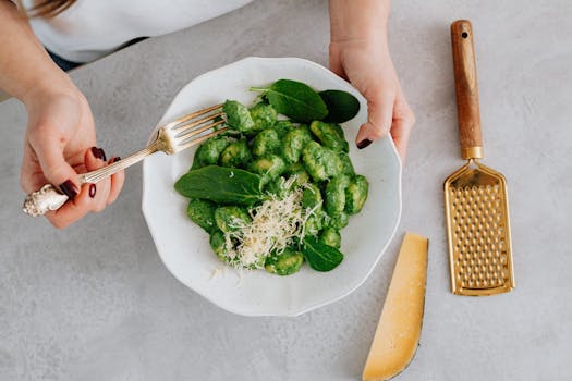 Gnocchis aux vitelottes avec sauce verte, servies dans une assiette blanche, garnis de fromage et de feuilles d'épinard.