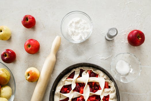 Pâté aux pommes maison avec des pommes rouges et jaunes, farine, sucre et rouleau à pâtisserie sur une surface de travail.