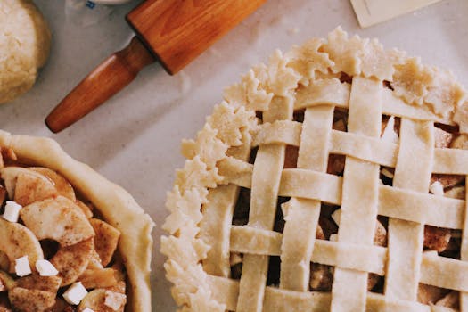 Deux tartes aux pommes maison, l'une avec une croûte tressée et l'autre garnie de pommes et de sucre. Un rouleau à pâtisserie
