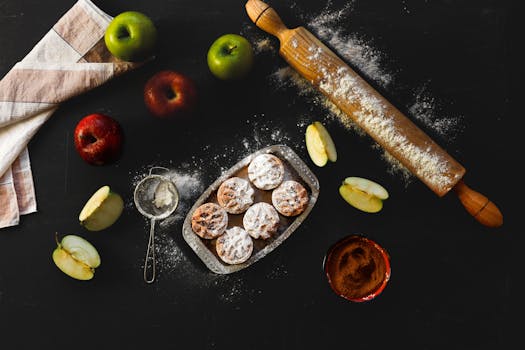 Pommes, rouleau à pâtisserie et tartelettes sur un plan de travail noir, avec de la farine et des tranches de pommes.