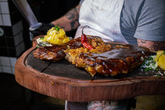 Plateau en bois avec travers de porc nappés de sauce BBQ, accompagnés de garnitures et d'une touche de piment.