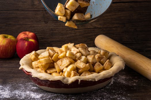Pommes coupées en dés ajoutées à une croûte de tarte au beurre, avec des pommes entières et un rouleau à pâtisserie en arrièr
