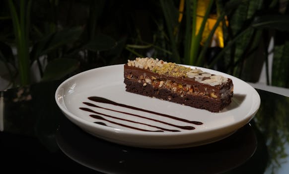 Partie d'entremets praliné-chocolat sur une assiette blanche, décorée de sauce chocolat et garnie d'amandes.