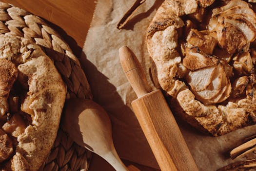 Tarte aux pommes maison sur une table en bois, avec un rouleau à pâtisserie et une cuillère en bois à côté.